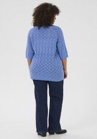 Pull en laine bleu clair avec un motif en losanges, à manches courtes et coupe ample, associé à un jean en denim noir.