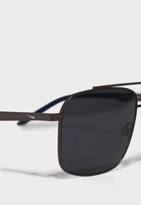 Gafas de sol de metal marrón con montura rectangular, lentes oscuros y acentos azules en las varillas. Presentan un pequeño logo en la patilla.
