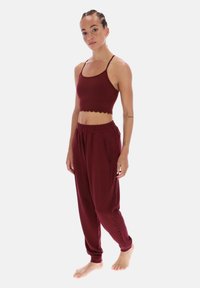 Top sportivo corto color bordeaux con orlo smerlato abbinato a pantaloni jogger a gamba affusolata, dotati di tasche laterali e vita elastica.