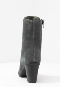 Stivaletto alla caviglia in suede grigio con una texture liscia, tacco alto e zip laterale, con un branding minimale nella parte superiore.