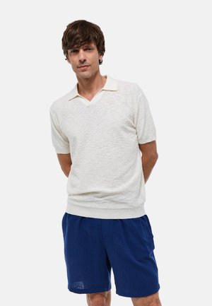 Polo shirt à manches courtes de couleur claire avec un tissu texturé, un design en V et un col contrastant, associé à un short bleu.