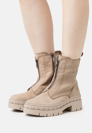 Bottes de cheville beiges en daim avec une semelle épaisse et crantée. Présente des zip apparents et une languette à l'arrière.