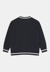 Námorně modrý svetr s bílými pruhovanými žebrovanými lemy a manžetami, dlouhé rukávy a textura pleteniny. Viditelný pohled zezadu.