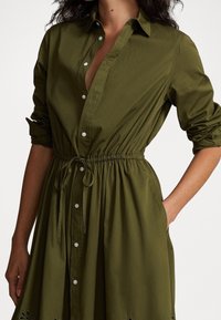 Olivgrön, knäppt klänning i lätt tyg med elastisk midja, med lång ärm och sidofickor.
