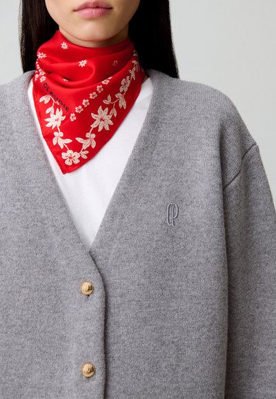 Cárdigan gris de punto con botones dorados, combinado con un pañuelo rojo con estampados florales blancos. Camisa blanca debajo.