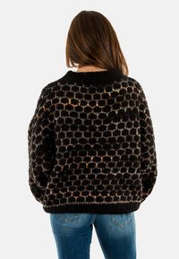Maglione nero lavorato a maglia con un motivo testurizzato di punti colorati, maniche larghe e scollatura rotonda. Abbinato a jeans blu.