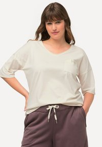 Creme kortærmet t-shirt med v-hals, som har en lille lommedetalje foran og en sløjfe. Sættes sammen med maroon sweatpants med snoretræk.