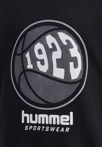Zwarte t-shirt met een ronde basketbalafbeelding en het jaar "1923" in het wit. De merknaam "hummel" is eronder gedrukt in witte letters.