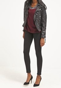 Giacca da moto in pelle nera, top borgogna con scollatura di perline, jeans skinny neri e scarpe col tacco nere. Texture liscia.