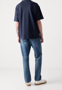 Marinblå bomulls t-shirt, avslappnad passform, kort ärm. Ljusblå jeans, rak passform, något blekta. Vita sneakers med gummisulor.