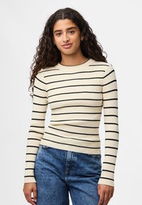 Ριγέ πουλόβερ μακρύ μανίκι σε κρέμ και μαύρο με ραβδωτή υφή. Στενή γραμμή με στρογγυλή λαιμόκοψη και μακριές μανσέτες.