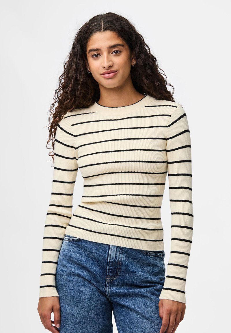 Ριγέ πουλόβερ μακρύ μανίκι σε κρέμ και μαύρο με ραβδωτή υφή. Στενή γραμμή με στρογγυλή λαιμόκοψη και μακριές μανσέτες.