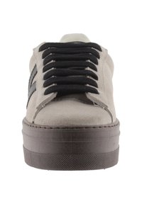 Beige mockasinsneaker med svarta snören, med en tjock brun gummisula och två svarta sidostrek. Minimalistisk design med rund tå.