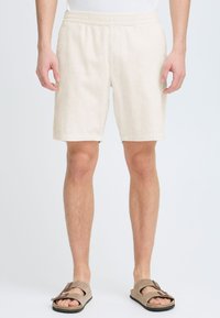 Kremfargede kordshorts med elastisk midje, knelange, med diskrete vertikale striper og bølget kant.