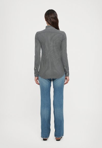 Chemise rayée noire et blanche avec des manches longues, poignets à boutons et un col pointu, portée avec un jean flare bleu clair. Vue de dos.