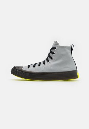 High-Top Sneaker mit grauem Canvas-Obermaterial, schwarzen Schnürsenkeln, gelber Außensohle und schwarzer Gummispitze; verfügt über eine Zuglasche an der Rückseite.