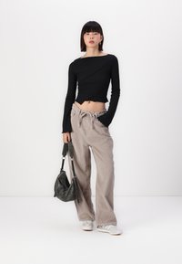 Haut noir à manches longues avec un design asymétrique, associé à un pantalon en velours côtelé large de couleur gris clair et un sac à main texturé de couleur gris foncé.