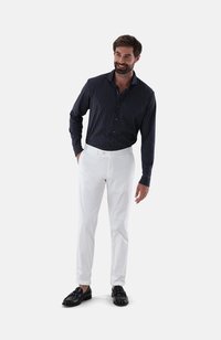 Marinegestreiftes Button-up-Shirt, weiße Hose und schwarze Slipper. Slim Fit; das Shirt hat einen Kragen und Manschetten. Die Hose ist schmal geschnitten mit einem umgeschlagenen Saum.