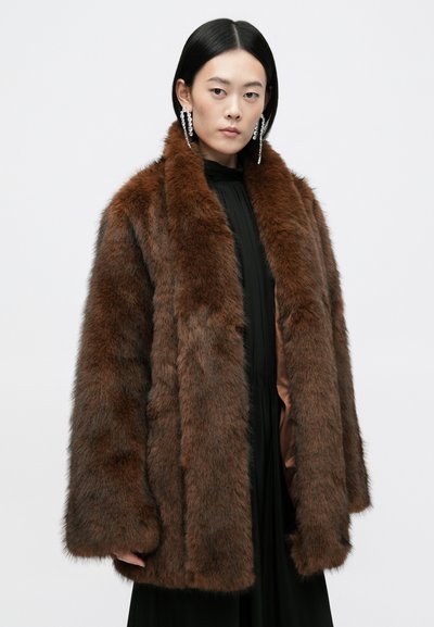 Abrigo de pelaje sintético marrón con un cuello ancho y mangas largas, que presenta una superficie suave y texturizada, y un corte relajado. Llevado sobre un vestido negro.