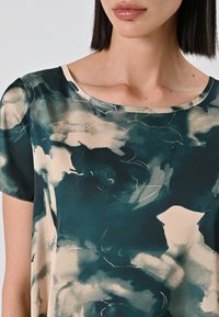 Blusa a fantasia floreale in tessuto morbido e leggero. Presenta colori verde scuro e crema con scollatura rotonda e maniche corte.