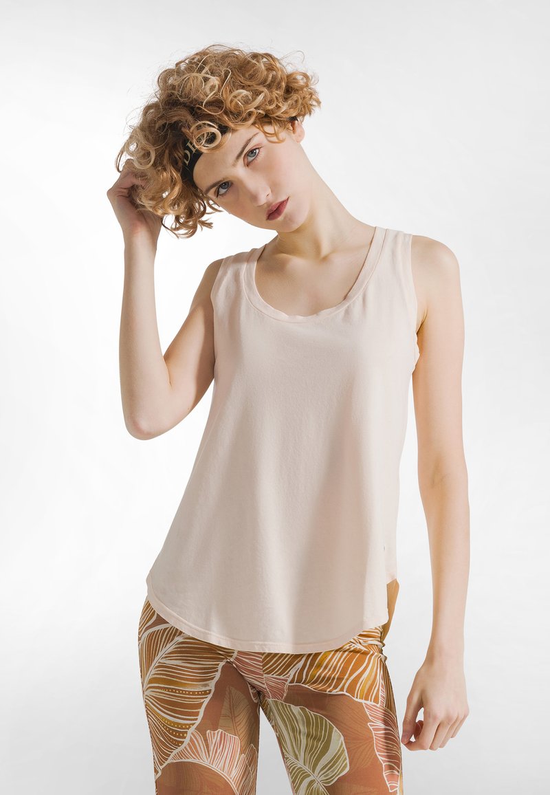 Top sin mangas color beige claro con escote redondo y bordes con ondas. Tela suave y lisa con un ajuste relajado, combinado con pantalones estampados.