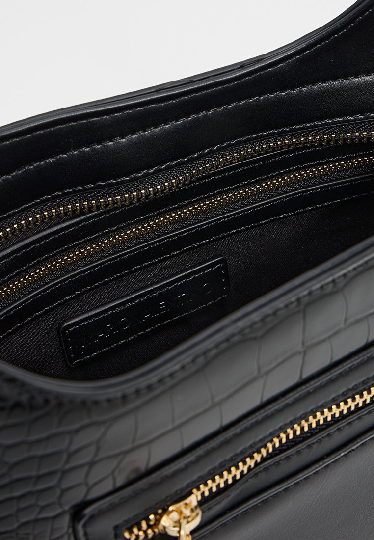 L'intérieur du sac à main noir dispose de plusieurs compartiments zippés, d'un cuir lisse, d'un motif crocodile texturé et d'accents en métal doré.