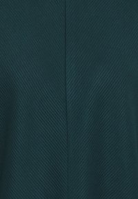 Texturiertes dunkelblaues Gewebe mit einem Fischgrätmuster. Die Oberfläche weist feine Erhebungen und vertikale Linien auf, die ein strukturiertes Erscheinungsbild erzeugen.