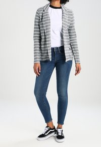 Grå och vit randig kavaj, vit t-shirt, blå skinny jeans och svarta sneakers. Kavajen har krage och framfickor.