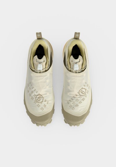 Ζευγάρι μπεζ sneakers χωρίς κορδόνια με λαστιχένιες σόλες και τυπωμένο σχέδιο με αριθμούς στην κορυφή, από ψηλά με φόντο λευκό.