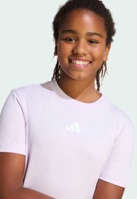 Jasnofioletowa koszulka z krótkim rękawem, wykonana z miękkiej bawełny, z małym białym logo w okolicach dekoltu. Gładka tekstura, okrągły dekolt.