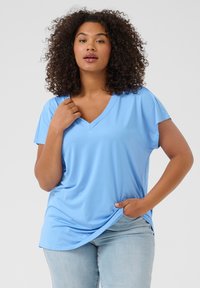 Light blue V-neck T-shirt made of soft, smooth fabric. Short sleeves with a relaxed fit and side slit detail. Worn with light denim jeans.