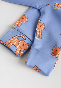 Maniche di tessuto blu con tigri dei cartoni animate arancioni e testo giallo. Texture liscia con polsini elastici. Le illustrazioni delle tigri sono ripetute.