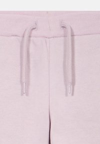 Világos rózsaszín melegítőnadrág bordázott derékpánttal és húzózsinórral. Puha tapintású, enyhén rugalmas. Nincsenek látható minták vagy további részletek.