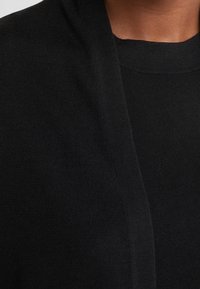 Schwarzes Stricktop mit gerundetem Halsausschnitt und offenem Design, das eine glatte Textur und keine sichtbaren Muster oder Akzente zeigt.