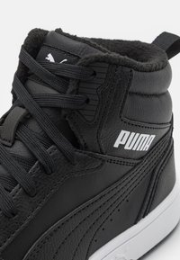 Baskets montantes noires Puma avec doublure en fourrure, logo Puma blanc sur le côté et lacets noirs, sur fond blanc.