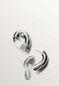 Los pendientes metálicos plateados presentan un diseño moderno con contornos suaves, acentos de acrílico transparente y un detalle de gema única.