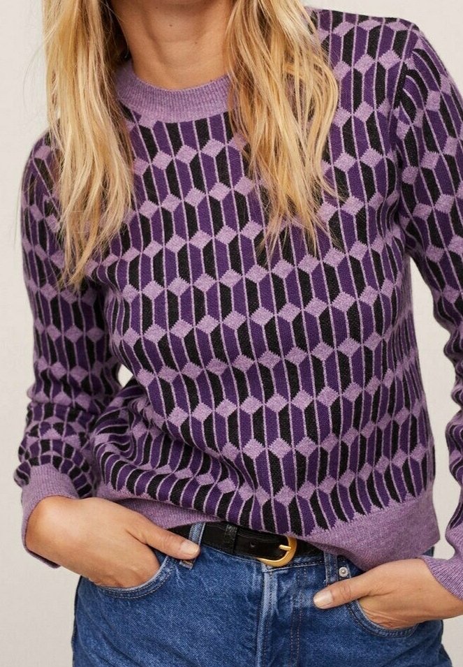 Maglione viola con motivi geometrici in tonalità di nero e lavanda, con scollo tondo e polsini a costine. Indossato con denim.