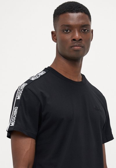 Svart bomull T-shirt med rund halsringning, korta ärmar och vit "Moschino"-logotyp längs axelsömmarna.