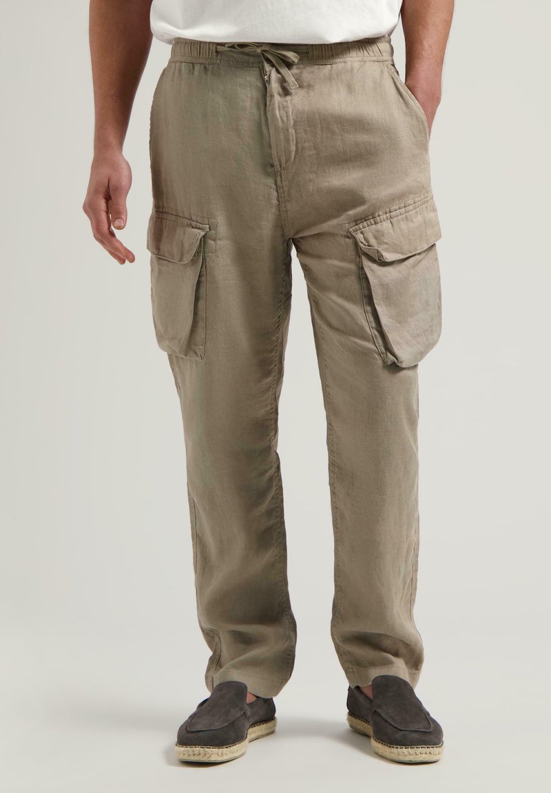 Khaki plátenné cargo nohavice s elastickým pásom, šnúrkou a dvoma veľkými bočnými vreckami. Nosí sa s šedými espadrilkami.