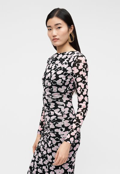 Vestido preto de mangas compridas com padrão floral em rosa e branco, corte justo, detalhe franzido na cintura. Modelo usa brincos grandes em forma circular.