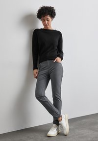 Zwarte trui met een ronde hals, gecombineerd met grijze tapered broeken met zijzakken, aangevuld met witte sneakers. Een soepele textuur in het geheel.