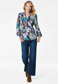 Bluse mit Floraldruck auf navy Hintergrund, mit langen Ärmeln, V-Ausschnitt und Raffung an den Schultern, kombiniert mit blauen Jeans.