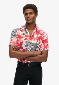 Korte mouwen shirt in rood en zwart bloemenpatroon, met een button-down kraag en zwarte hardware. Draagt het met zwarte jeans en een riem.