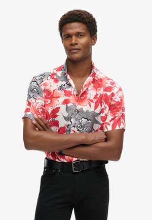 Korte mouwen shirt in rood en zwart bloemenpatroon, met een button-down kraag en zwarte hardware. Draagt het met zwarte jeans en een riem.