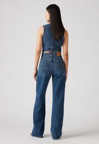 Blå denim crop-top med frynsete kanter og høytlivs vide jeans med lommer bak og en lærmerke med merkevaren.