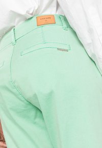 Calças de algodão verdes menta com um rótulo de couro a dizer "cream" na parte de trás da cintura. As características incluem um design ajustado e costuras detalhadas.