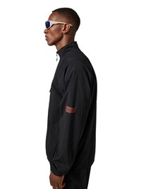 Person in black zip-up jacket with a brown patch on the sleeve, wearing white-framed sunglasses, facing left against a white background.