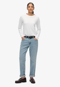 Witte overhemd met lange mouwen, lichtblauwe spijkerbroek met opgerolde boorden, zwarte riem en bordeauxrode loafers met een gestructureerde lederen afwerking.