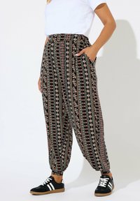 Persoon in hoge taille bloemenpatroon broek met elastische boorden, een witte top met korte mouwen, en zwarte sneakers met witte strepen.
