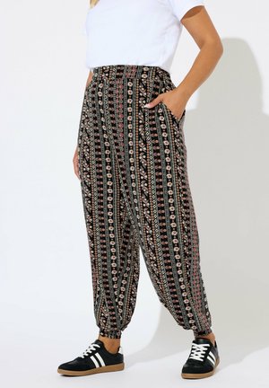Persoon in hoge taille bloemenpatroon broek met elastische boorden, een witte top met korte mouwen, en zwarte sneakers met witte strepen.